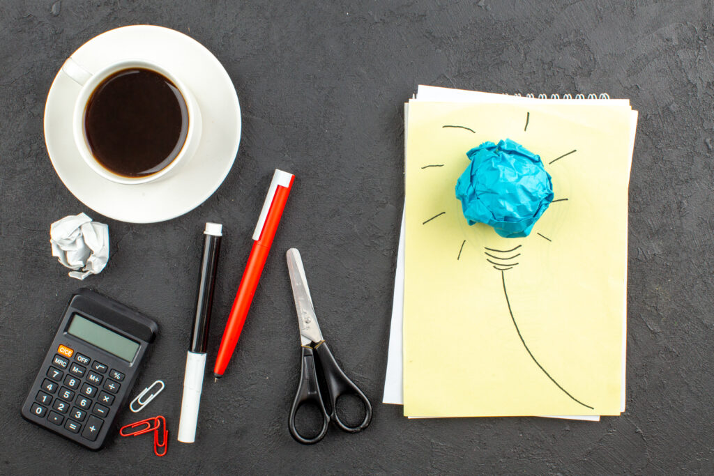 top-view-idealight-bulb-notepad-scissors-calculator-cup-tea-red-pen-black-marker-black